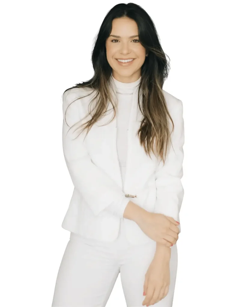 Fotografia de corpo inteiro da Dra. Amanda Caruso, médica focada em emagrecimento definitivo e reestruturação metabólica, sorrindo e posando com os braços cruzados contra um fundo branco isolado. Ela veste um blazer e calças brancas elegantes. A imagem transmite a confiança e a modernidade de seu atendimento médico humanizado.